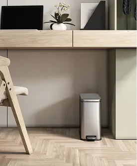 Modern stainless steel step trash can placed under a wooden desk in a contemporary home office.