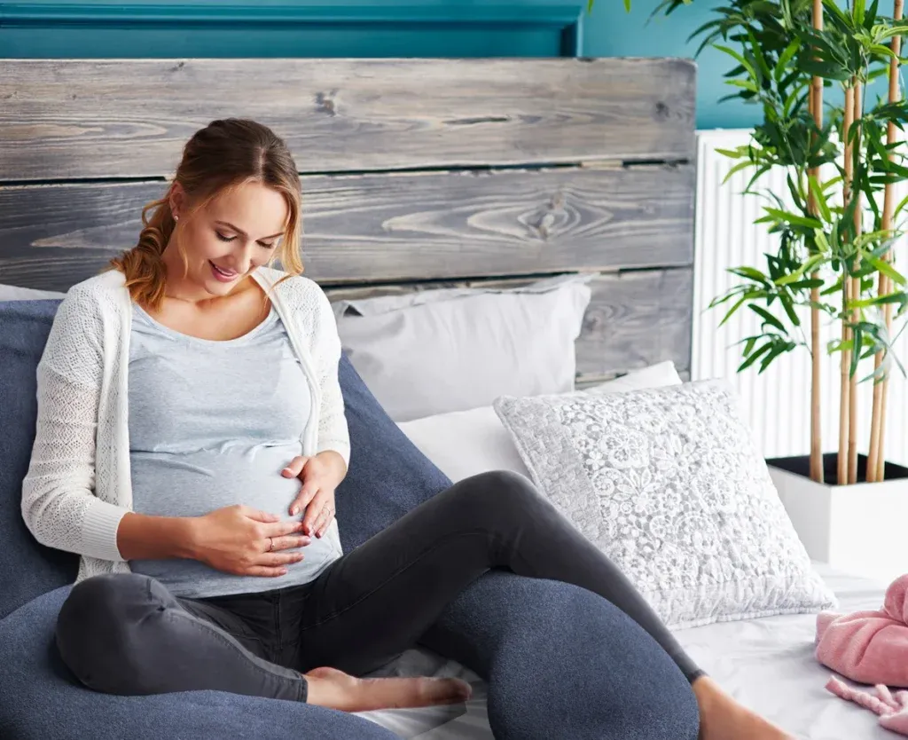 Photorealistic 3D product rendering of a maternity support pillow integrated into a lifestyle bedroom scene with a pregnant woman.