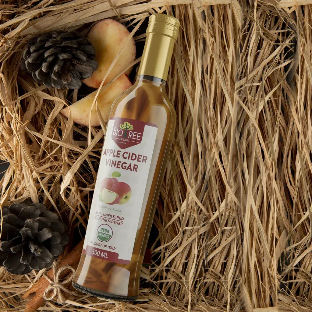 Rustic 3D packaging rendering of a Bio Ree organic apple cider vinegar bottle nestled in straw with pinecones and apple slices.