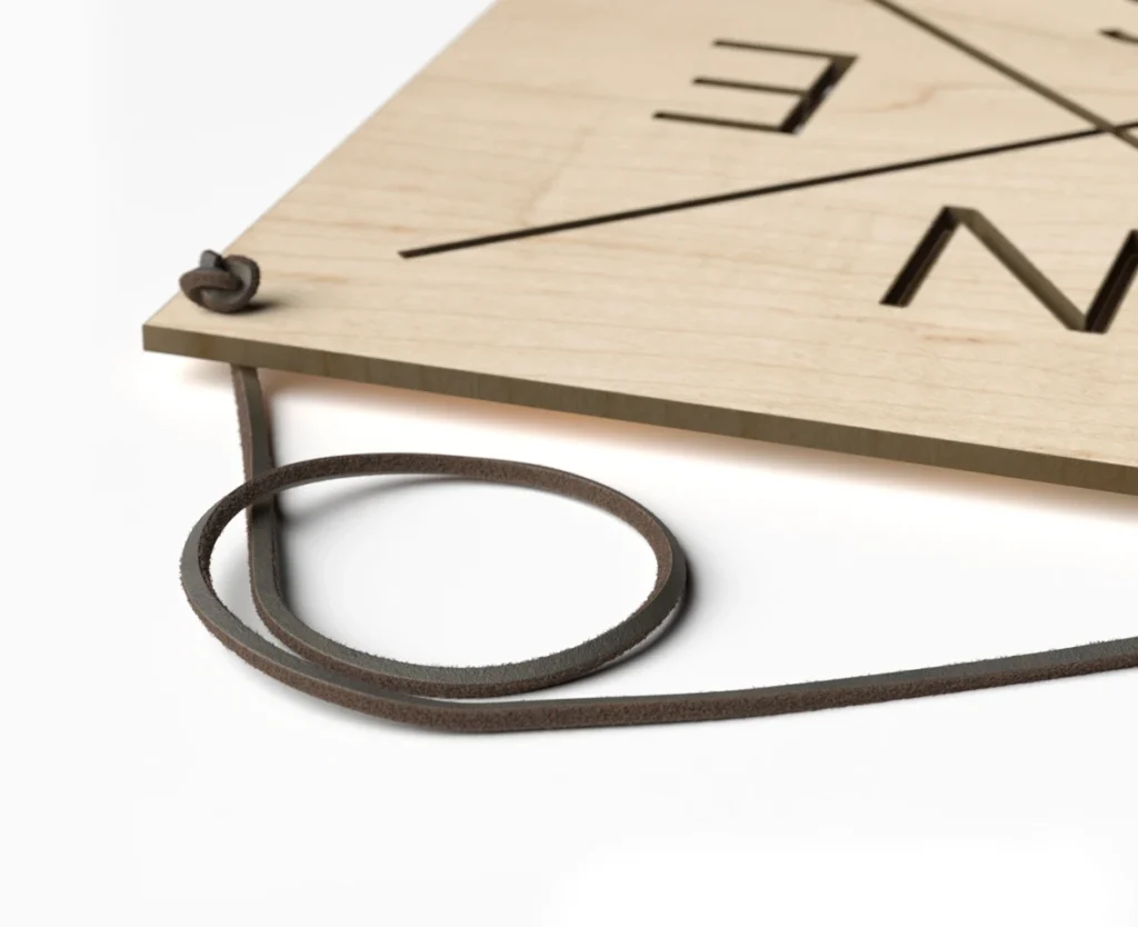 Extreme close-up 3D render of a wooden compass board showing realistic wood grain textures, CNC-cut lettering, and a dark brown leather hanging cord against a white background.