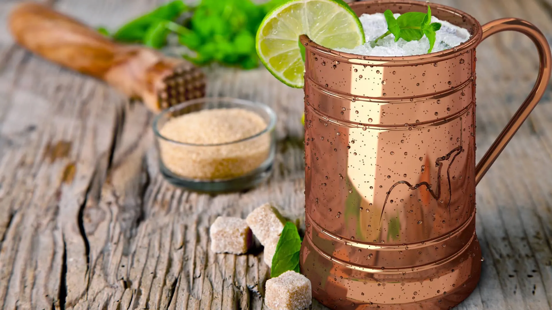 Copper mug with a crushed ice cocktail, lime slice, and mint leaves on a rustic wooden table
