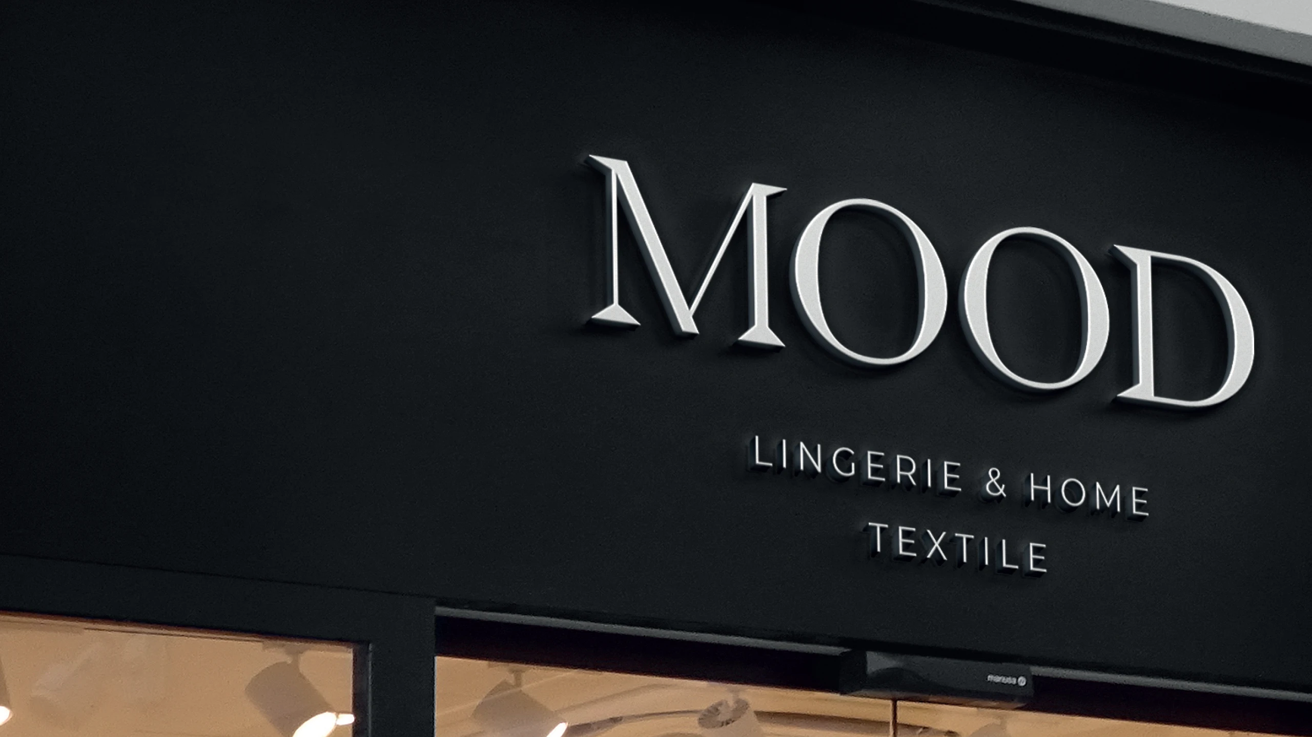 Mood Lingerie and Home Textile elegant white 3D serif logo design on a modern matte black storefront facade.